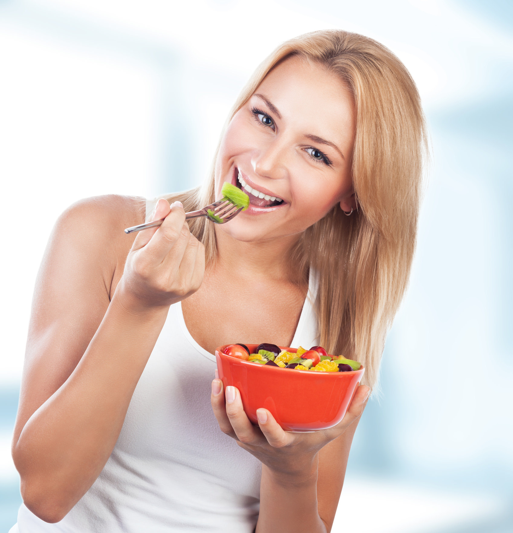 Portrait of pretty blond woman eating fresh tasty fruit salad on the kitchen at home, special fruity diet, enjoying organic nutrition and healthy lifestyle