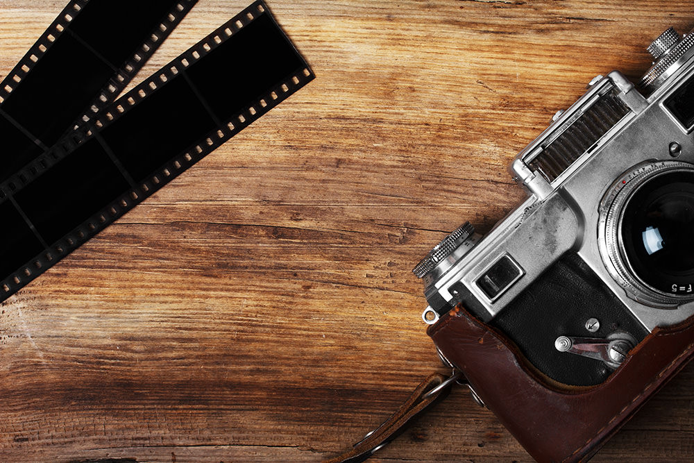 old camera and blank film strip on wooden table