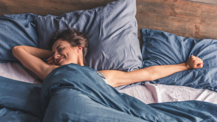 Beautiful young woman is stretching and smiling while lying in bed in the morning