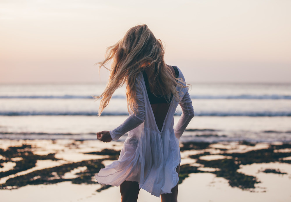 Beautiful blonde girl with long hair in short white dress dancing at sunset